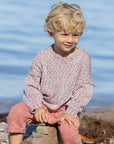 Child sitting on a log by the water in organic cotton Disana confetti sweater