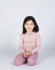 Girl sitting in Engel kids thermal layer made of 100% wool in rose-natural stripe.