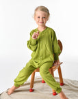Child wearing Cosilana wool terry footless pajamas in green sitting on chair