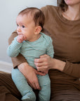 A baby wearing a serendipity organic cotton ivy striped long sleeve footed baby suit sits on an adult's lap.