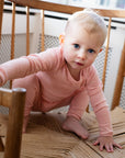 A baby on a chair wearing Serendipity's organic cotton coral bodysuit with matching baby leggings