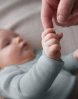 baby in slate blue bodysuit holding adult finger