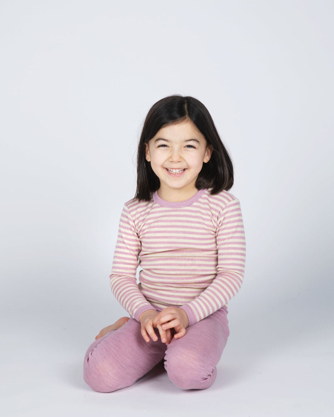 Girl sitting in Engel kids thermal layer made of 100% wool in rose-natural stripe.