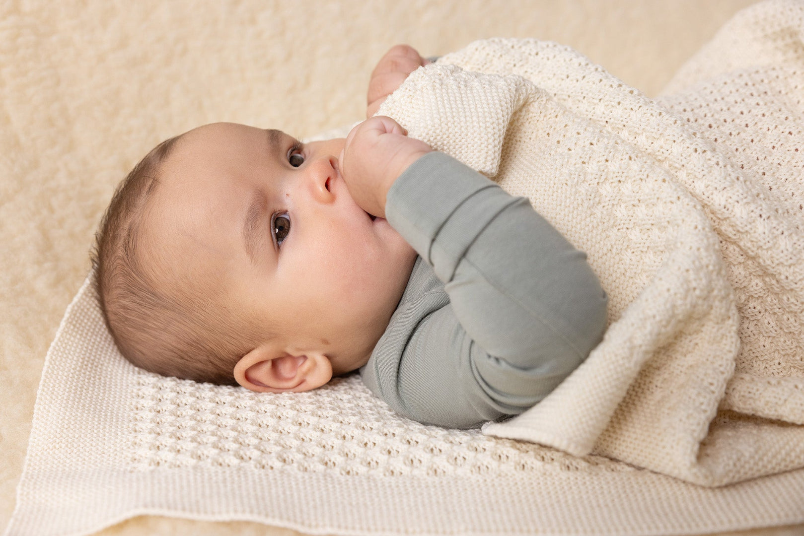 Lifestyle photo of a baby in Disana&#39;s organic merino wool honeycomb blanket in natural. 
