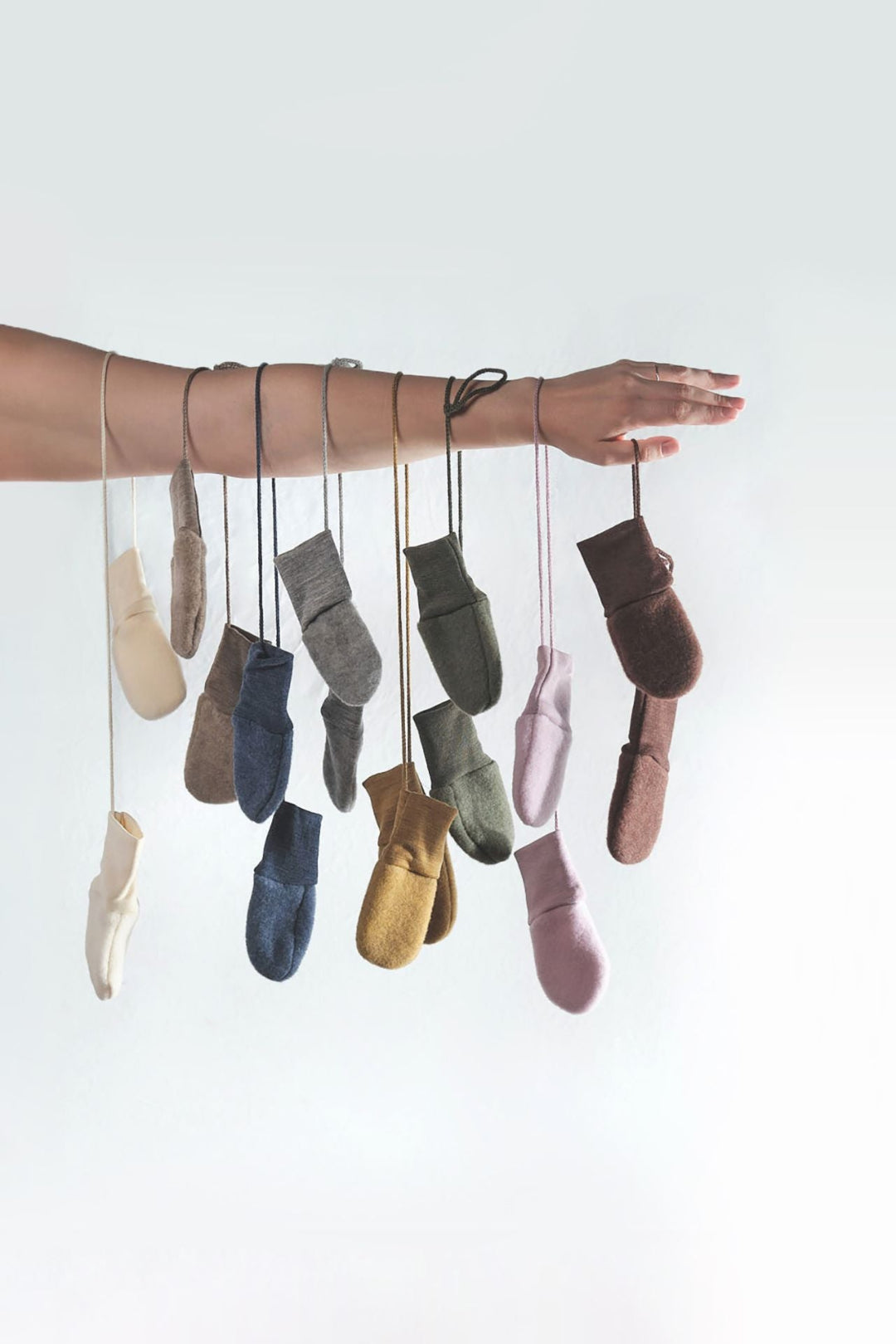 Set of Engel wool fleece baby mittens hanging from a woman's arm