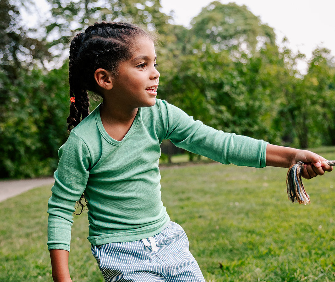Child in a Hocosa wool/silk shirt and striped pants playing outdoors with a kite string.
