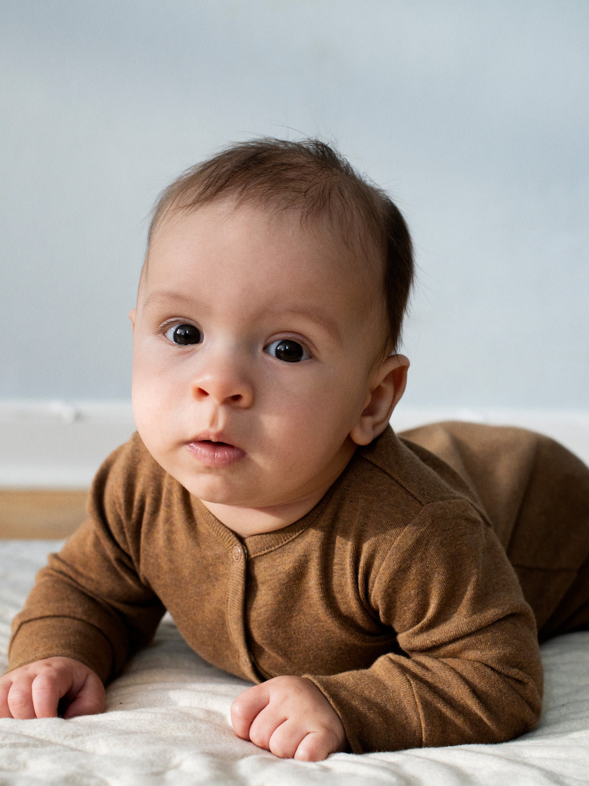 Baby on its stomach wearing a Serendipity organic cotton long sleeved almond overall