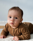 Baby on its stomach wearing a Serendipity organic cotton long sleeved almond overall