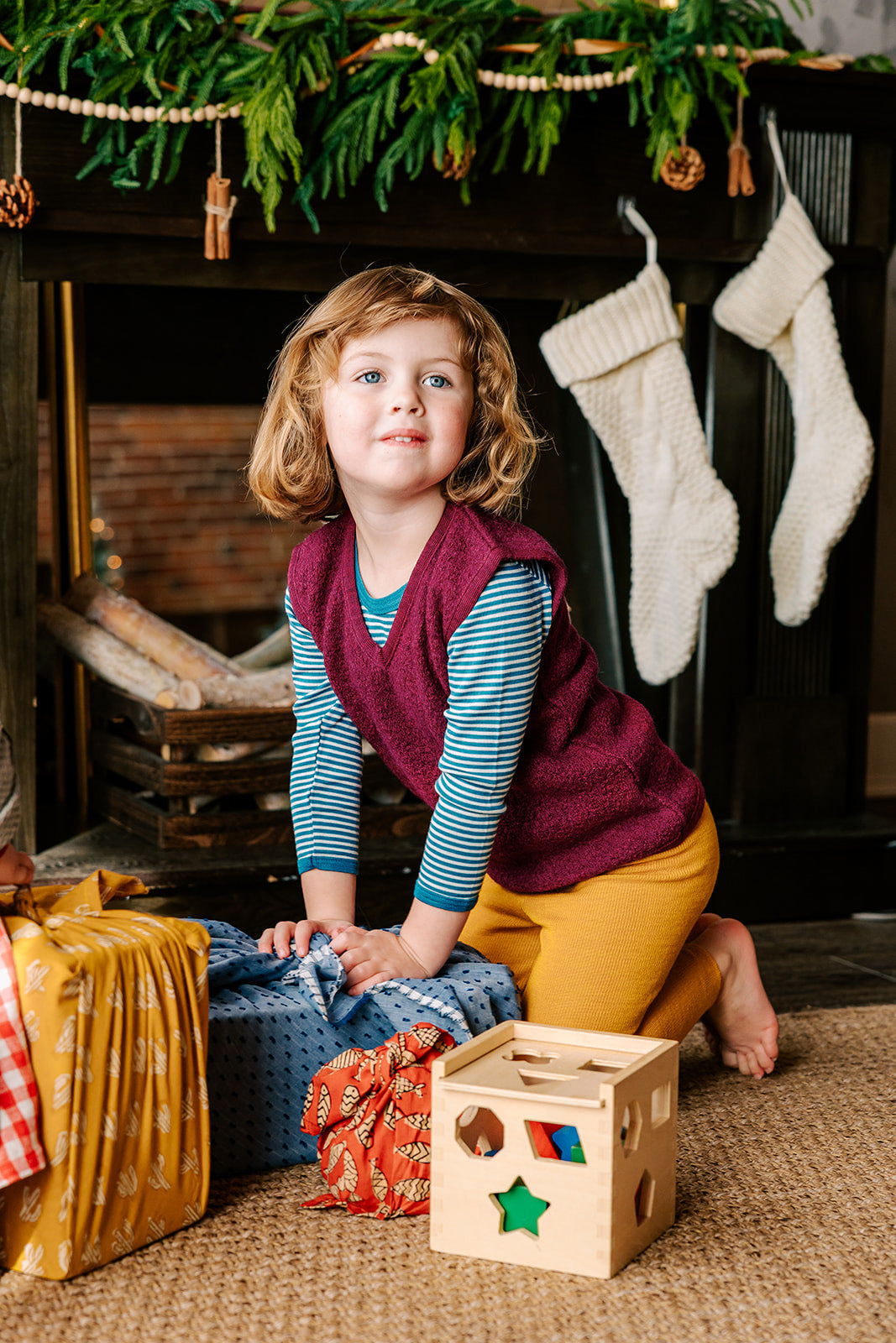 Girl opening presents in her Reiff wool vest in berry. Also wearing Reiff wool leggings in marigold