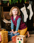 Girl opening presents in her Reiff wool vest in berry. Also wearing Reiff wool leggings in marigold