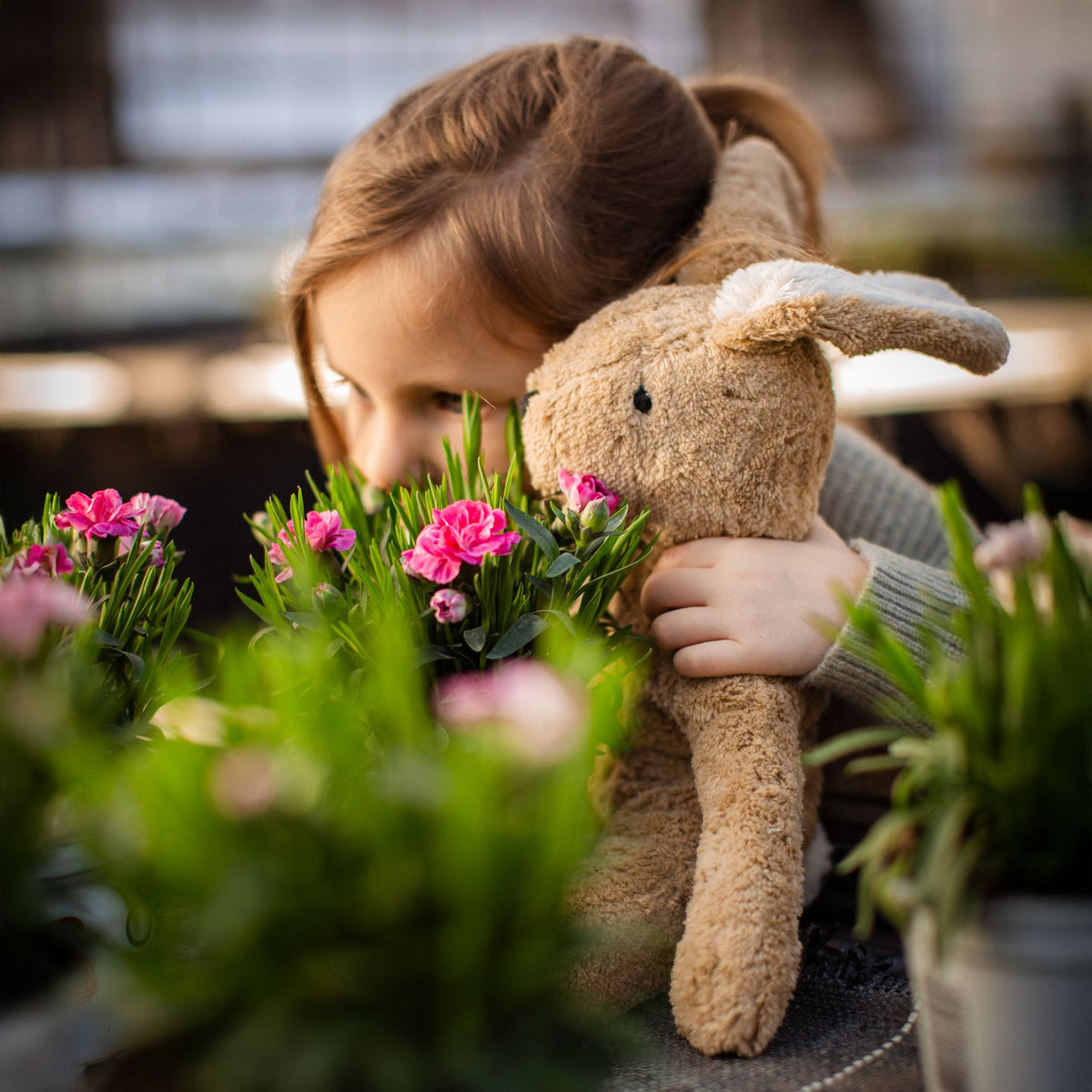 Young girl looking at plants holding Senger organic cotton non-toxic floppy small beige rabbit