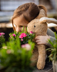 Young girl looking at plants holding Senger organic cotton non-toxic floppy small beige rabbit