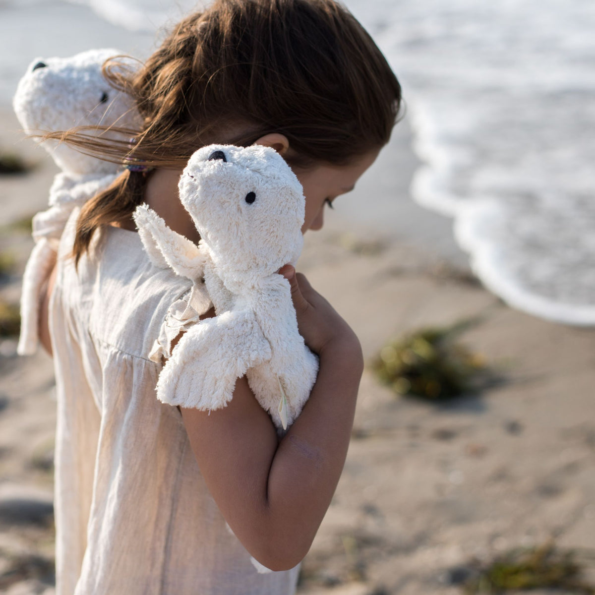 Young girl holding a Senger organic cotton non-toxic Cuddly small white seal on each shoulder
