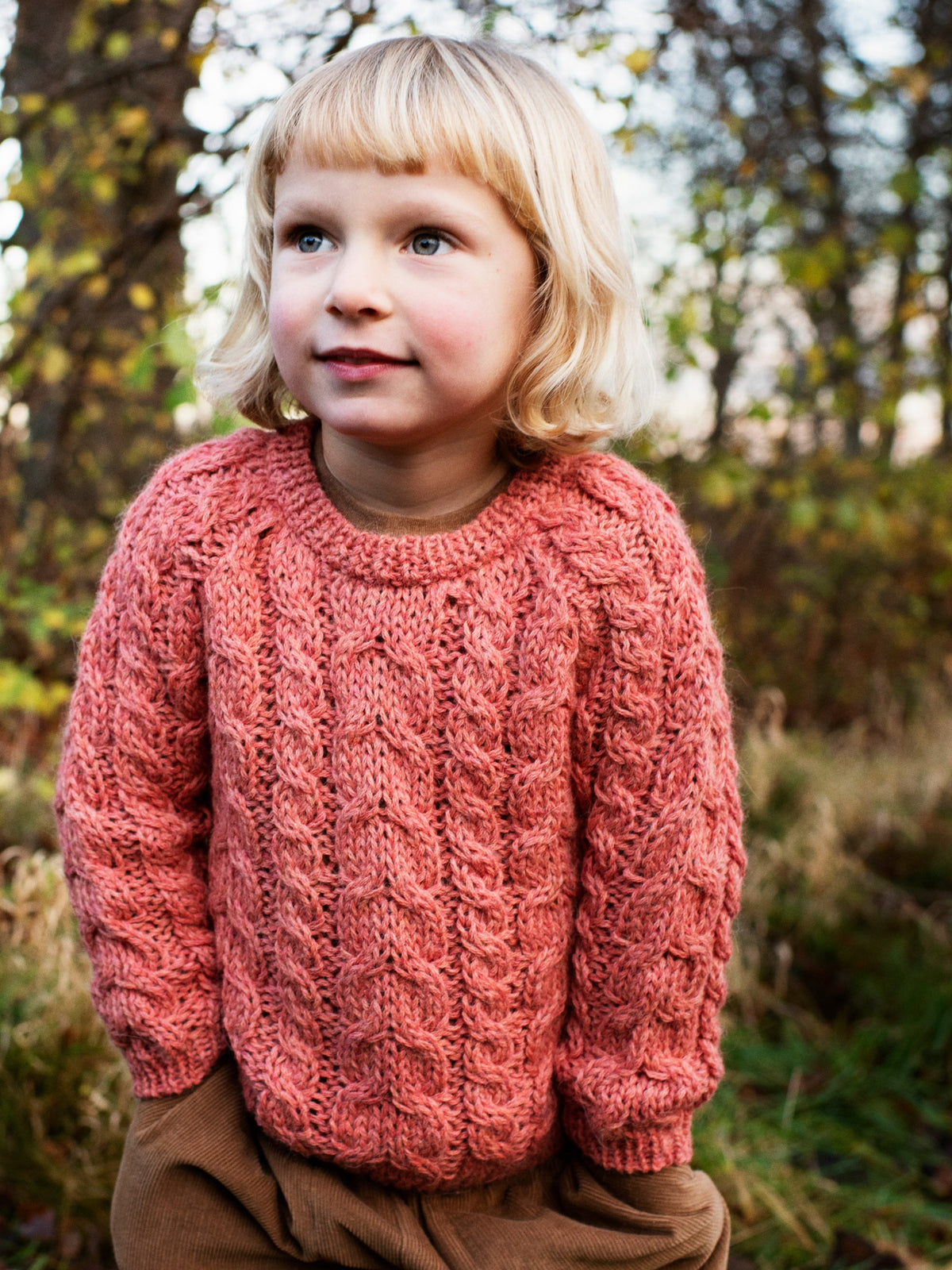 Girl wearing the Serendipity Organics alpaca cable sweater in coral