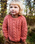 Girl wearing the Serendipity Organics alpaca cable sweater in coral