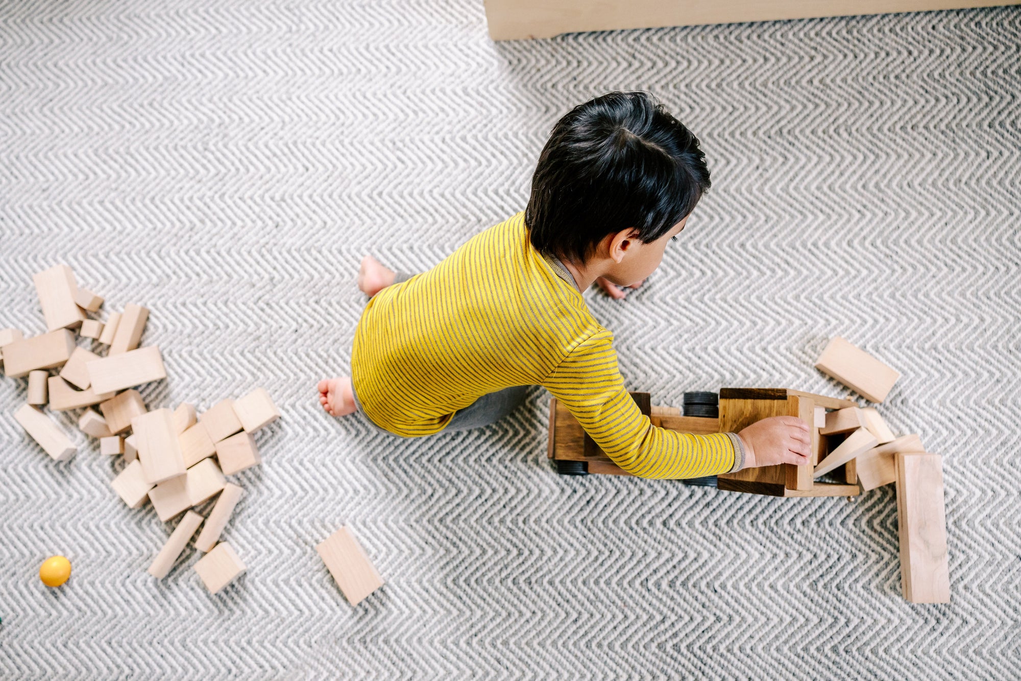 Child playing with wooden blocks in wool/silk base layers by Engel