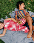 Girl lying in grass in a red Linenfox gingham linen jumpsuit